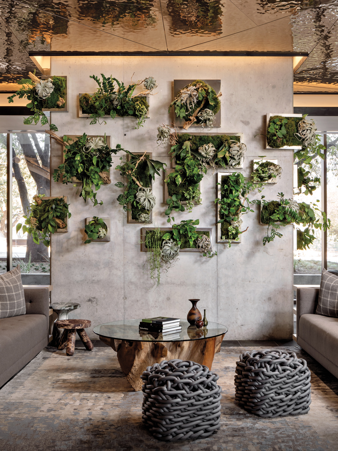 Gray-toned seating area centered by concrete wall with building planters with greenery growing out