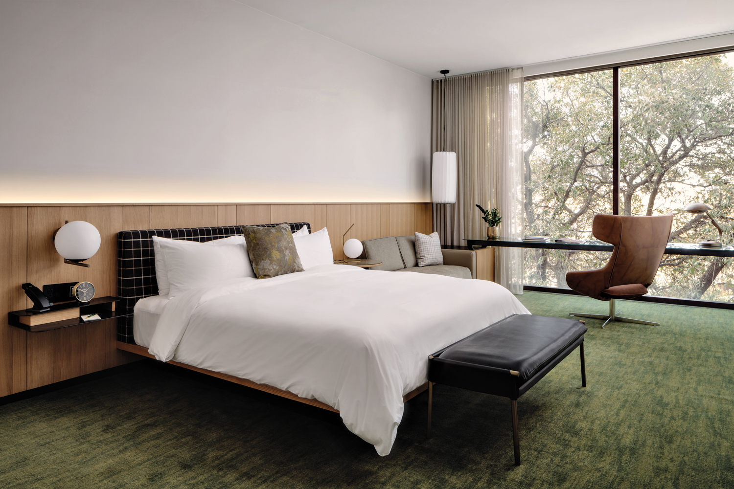 The Loren at Lady Bird Lake bed on dark green carpet parallel to floor-to-ceiling windows lined by a desk