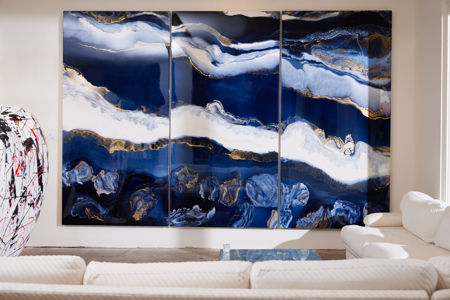 a large blue-white-and-gold abstract triptych in front of a white sofa