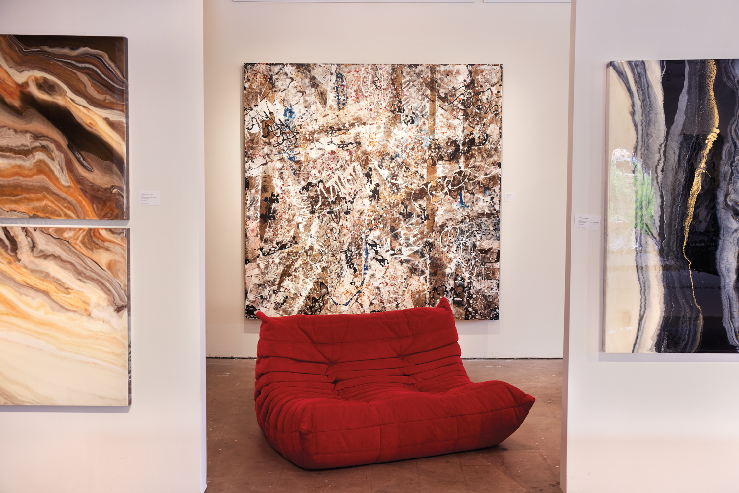 a red loveseat sits in front of a large abstract painting