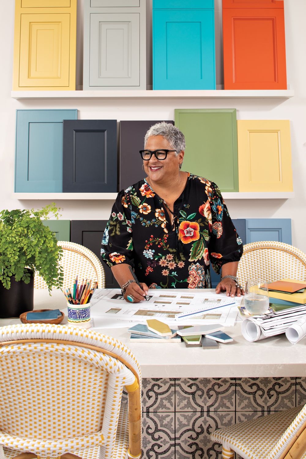 Caren Rideau standing over a work table with colorful cabinetry samples on a shelf behind her