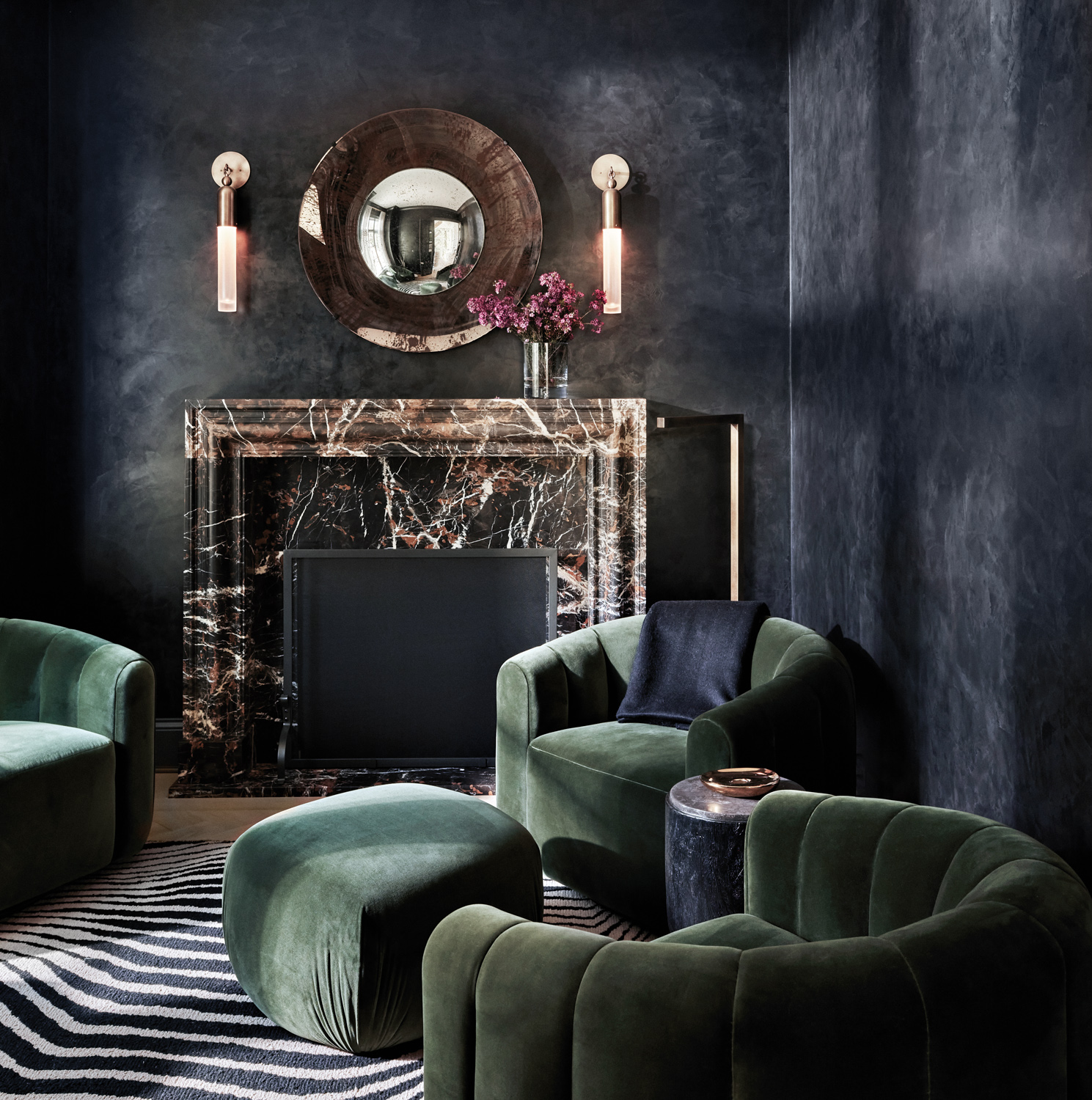 a cocktail room with black Venetian plaster alls, green velvet seating and a dark-veined fireplace