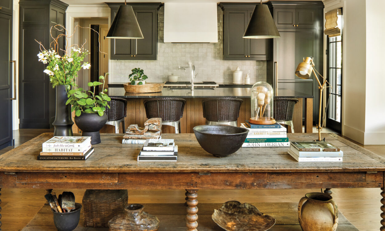 antique wooden table backed by a kitchen with black cabinetry and pendant lights over an island