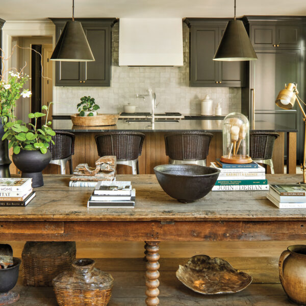 antique wooden table backed by a kitchen with black cabinetry and pendant lights over an island
