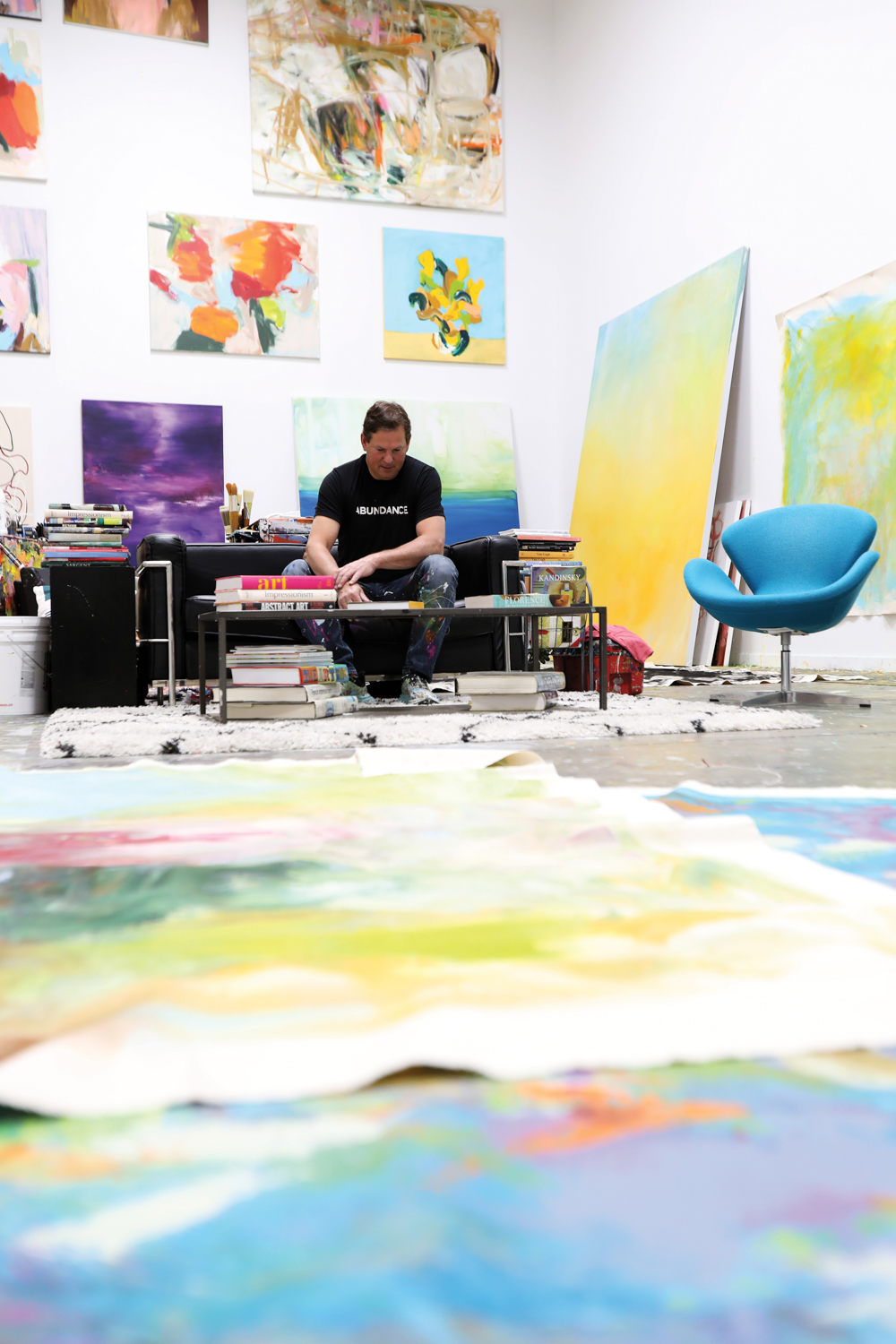 person sitting on couch in art studio, with a paint splattered canvas spread on the floor in front of them