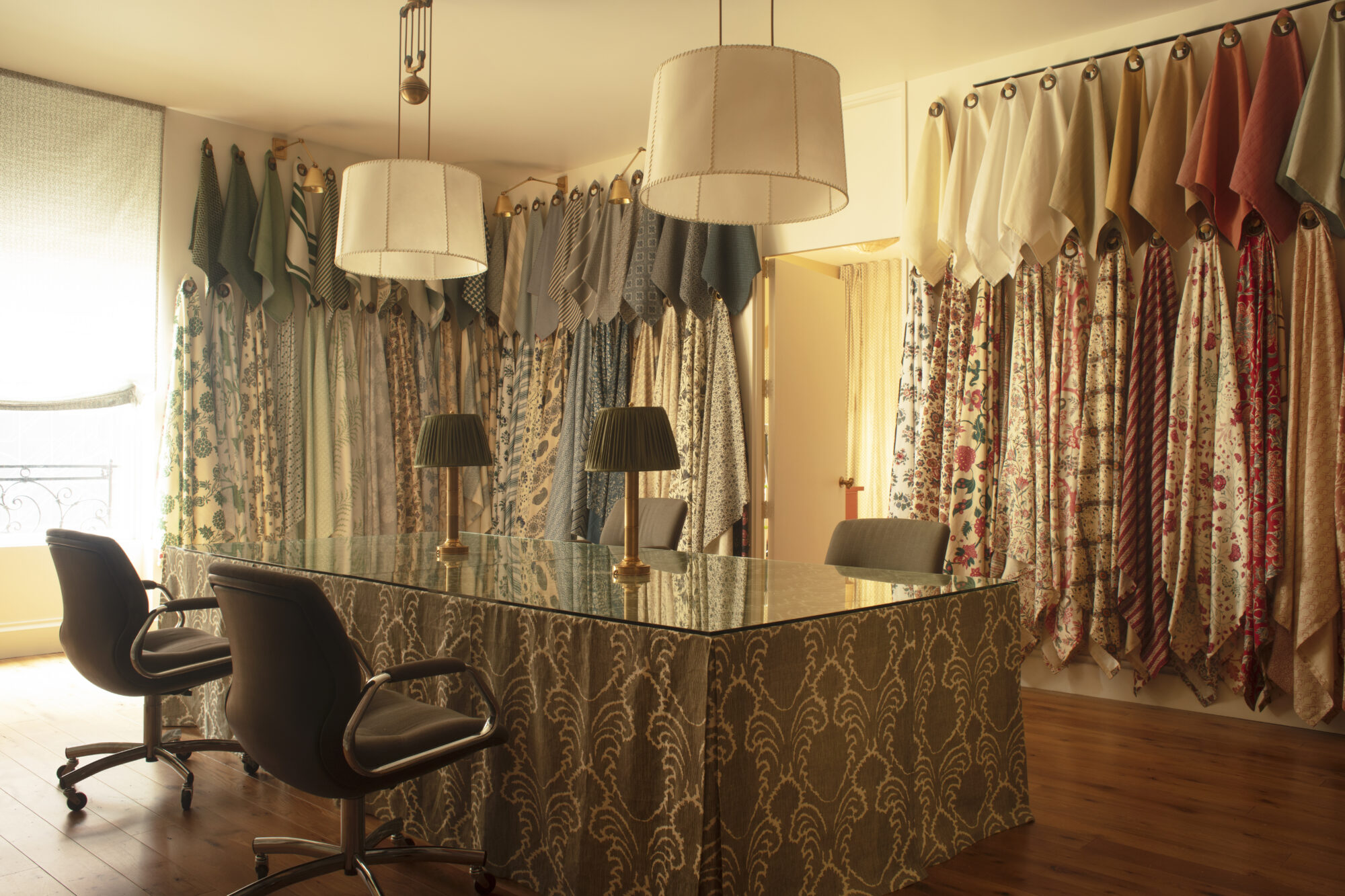 Drapes of patterned linens on display on the walls of a room with a skirted table at Soane Britain showroom