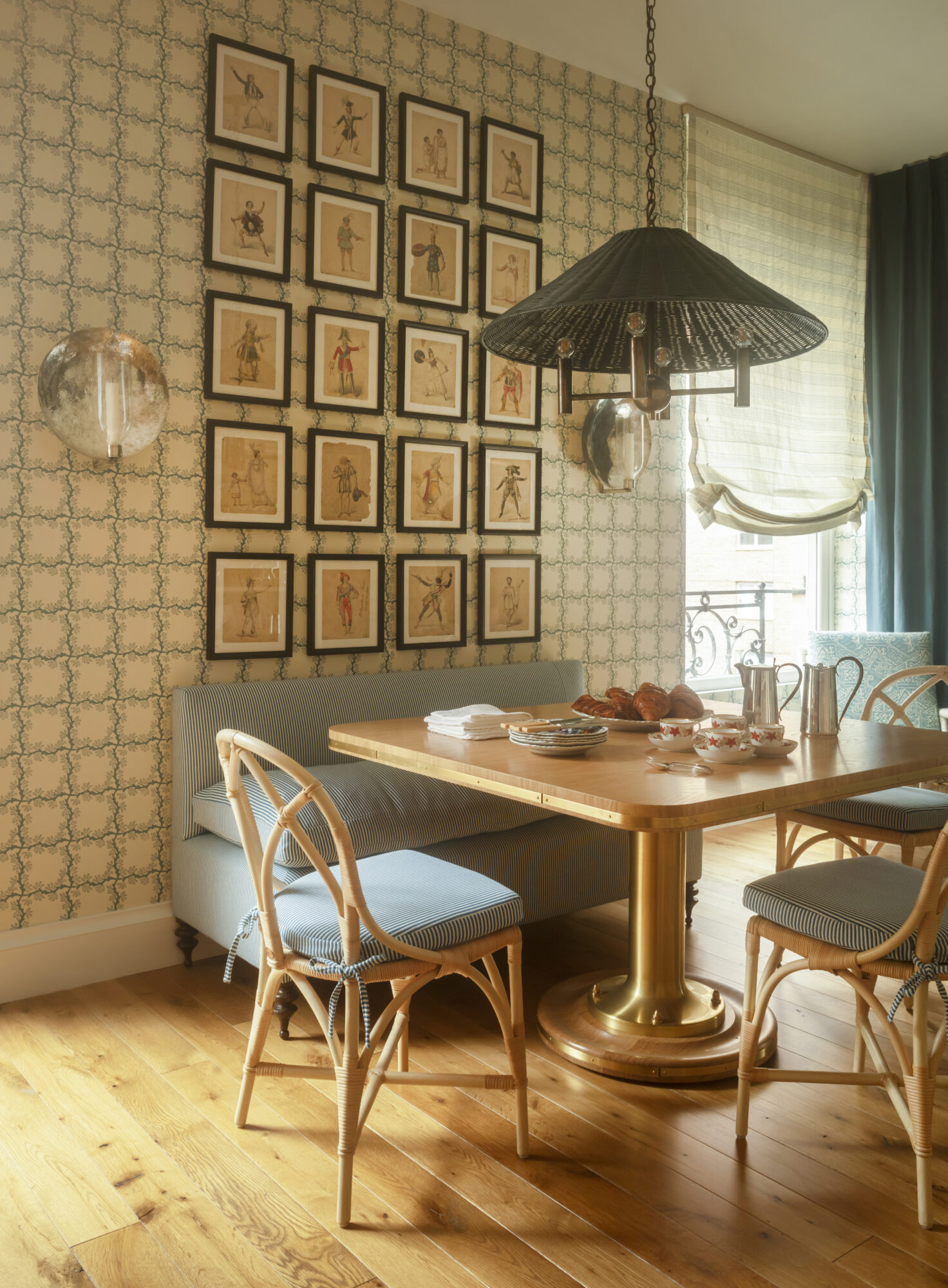 Breakfast nook with patterned wallpaper, rattan chairs, a pleated pendant light and a mosaic of small artworks