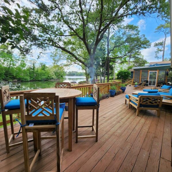 A serene patio featuring teak outdoor furniture, including a patio bistro set against a backdrop of lush greenery at a lake house