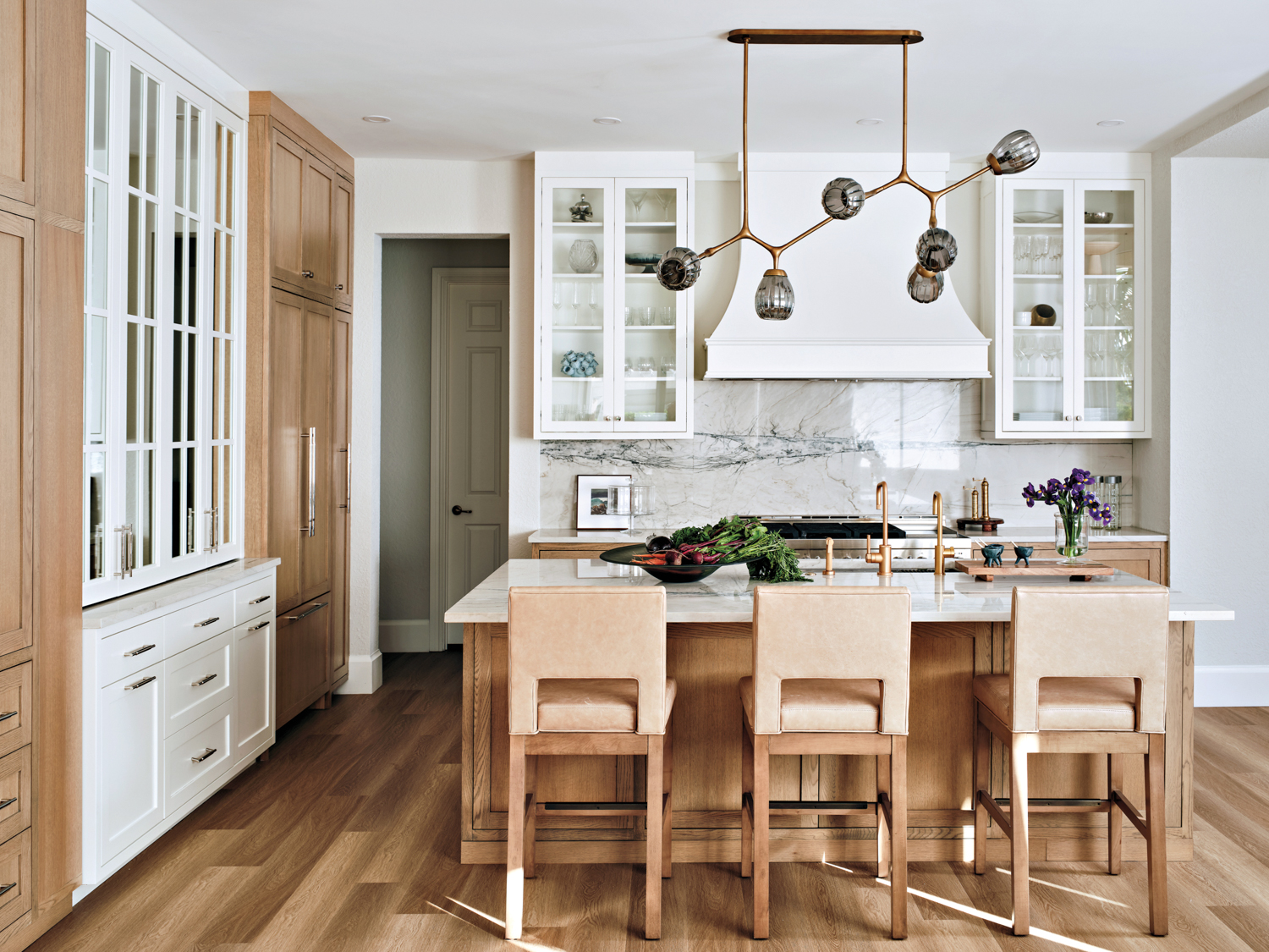 Kitchen with wood floors, island and chairs balanced with white cabinetry, a marble backsplash and a chandelier