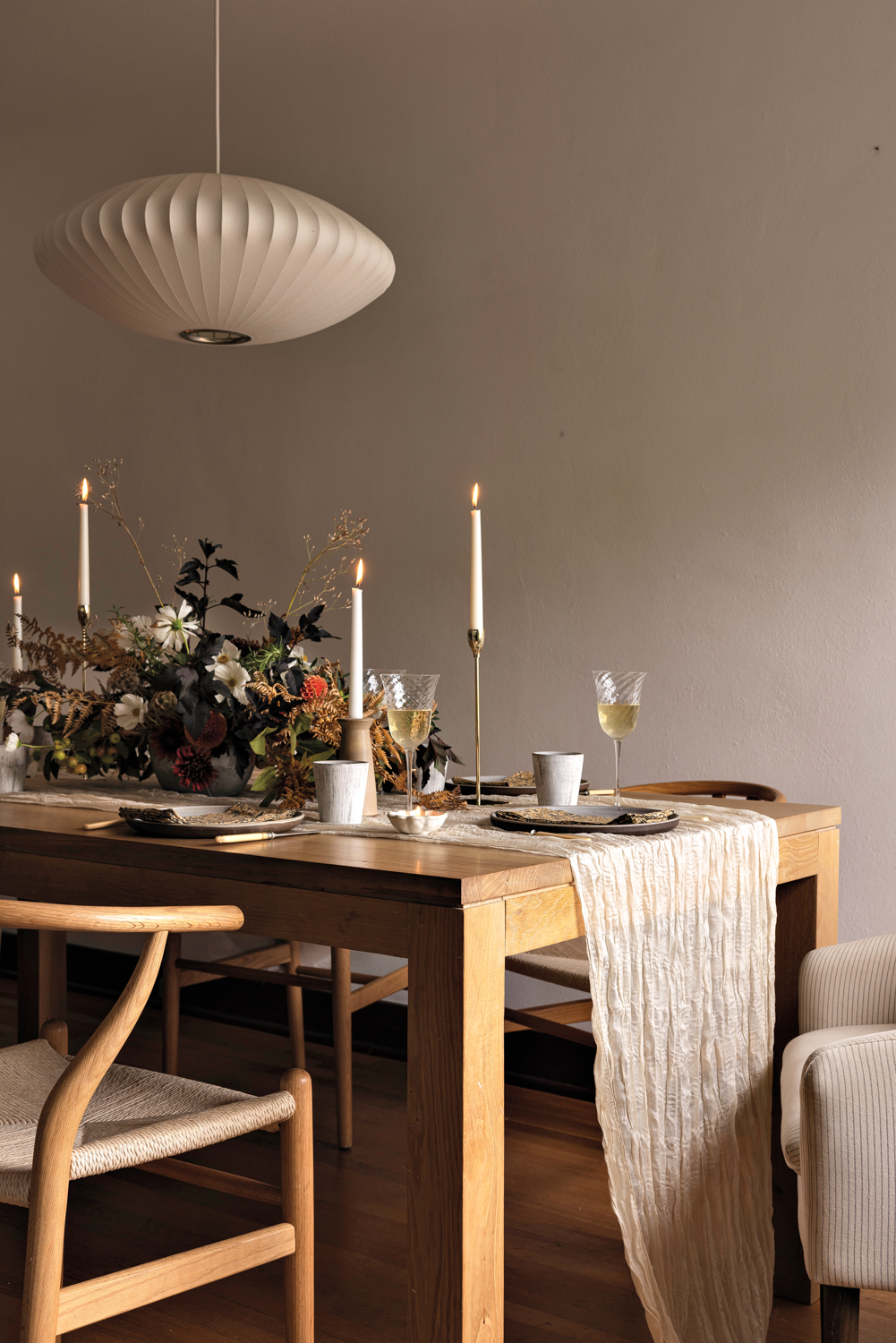 Wood dining table set with a light-colored cloth runner, candlesticks and a floral arrangement by Chloe Deane