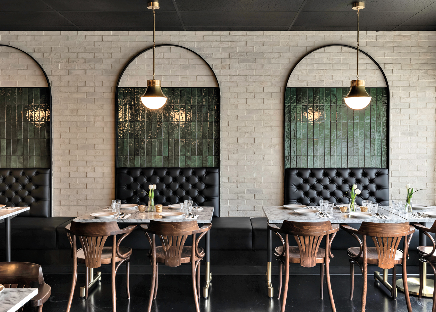 Ayesha Usman restaurant with cream and dark green tile, black tufted banquettes, wood chairs and pendant lighting