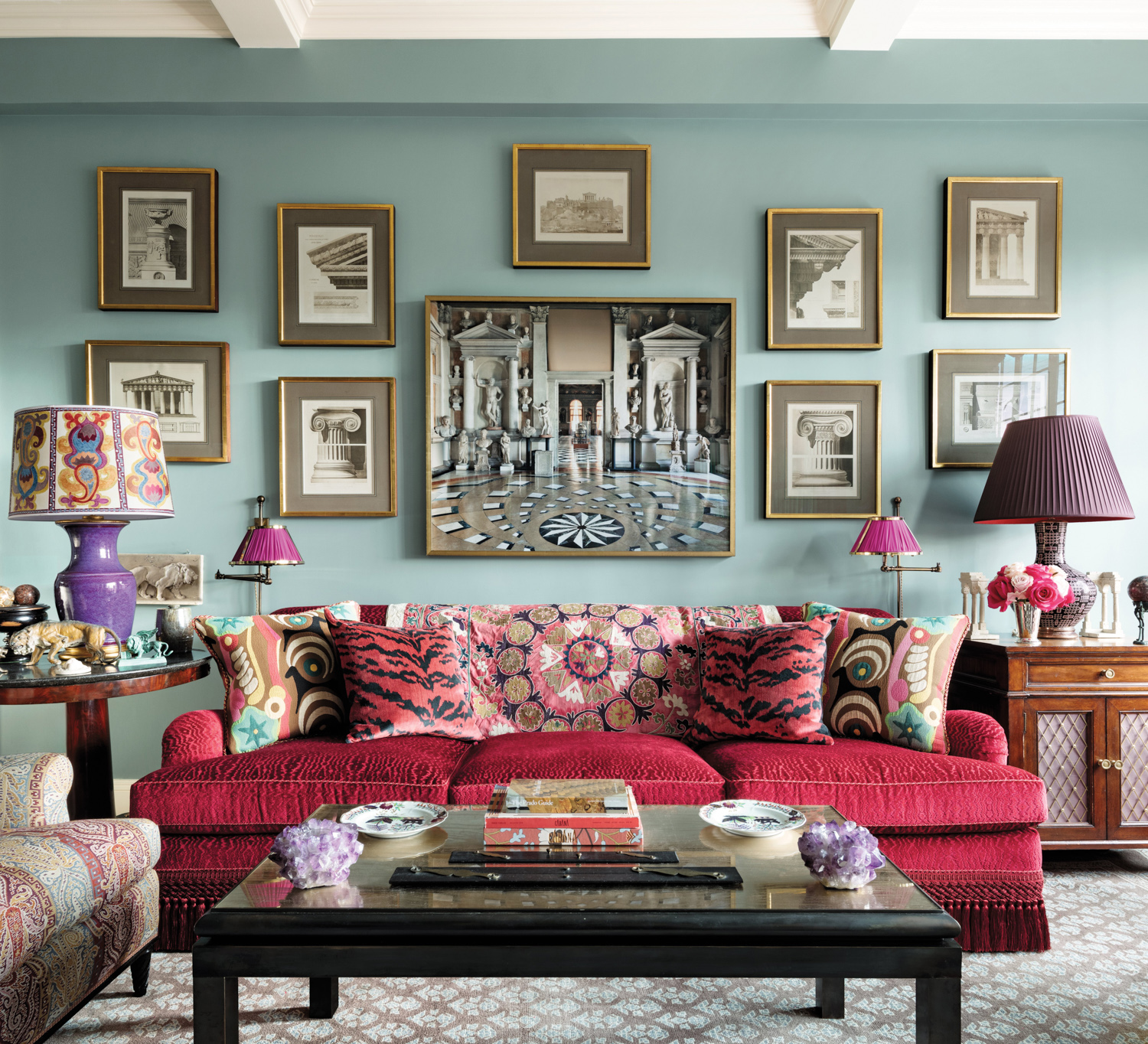 Maximalist seating area with pink patterned sofa in front of a mint-colored wall featuring various artworks.