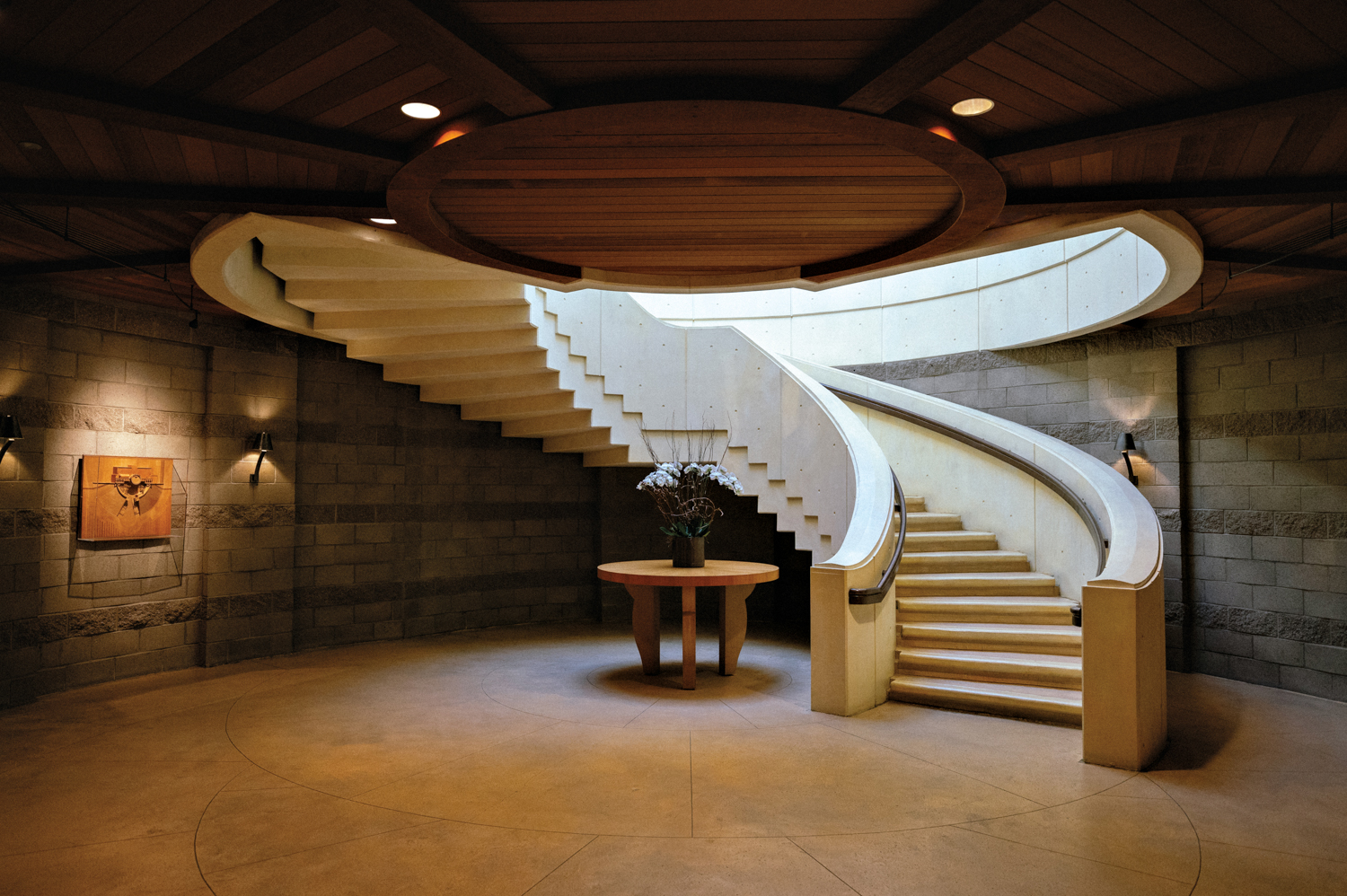 Opus One with stone walls, a round wood coffee table, artwork, moody lighting and a curved staircase