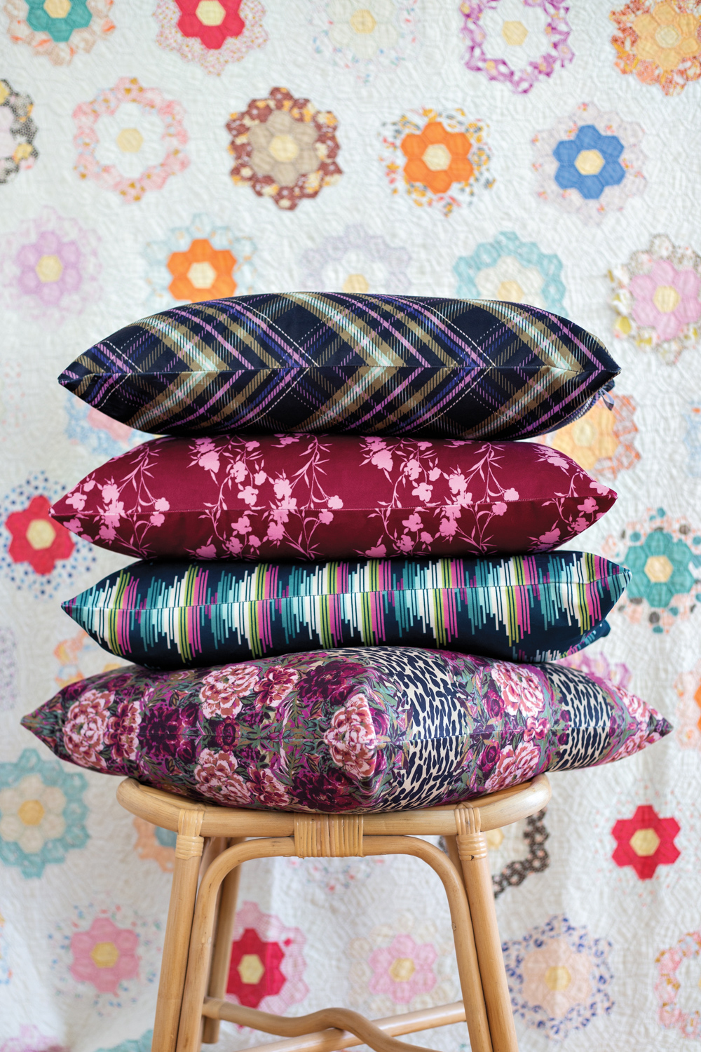 4 boldly patterned throw pillows stacked on a stool against a colorful background