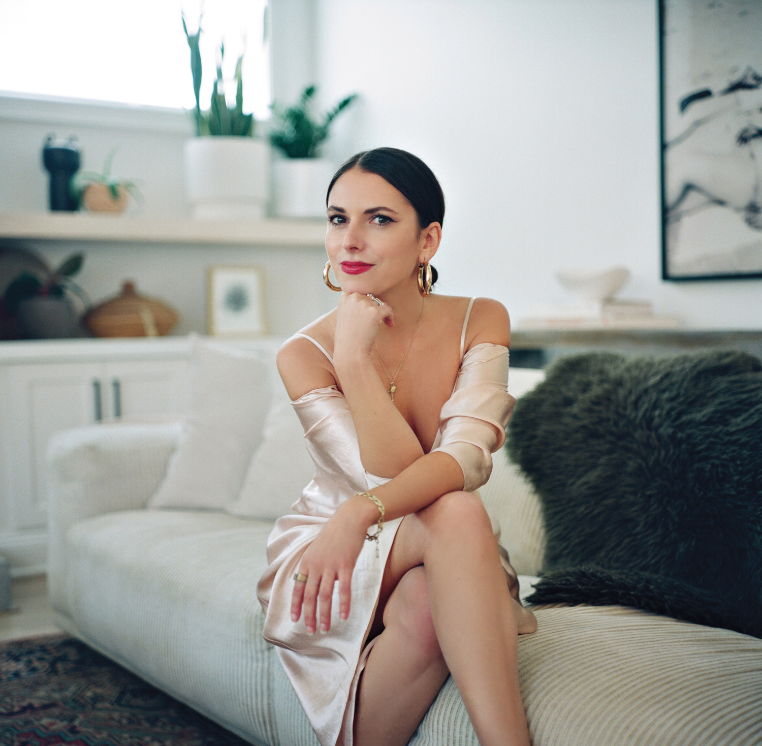 Jessica Maros sitting on a cream couch in a cream silky dress. 