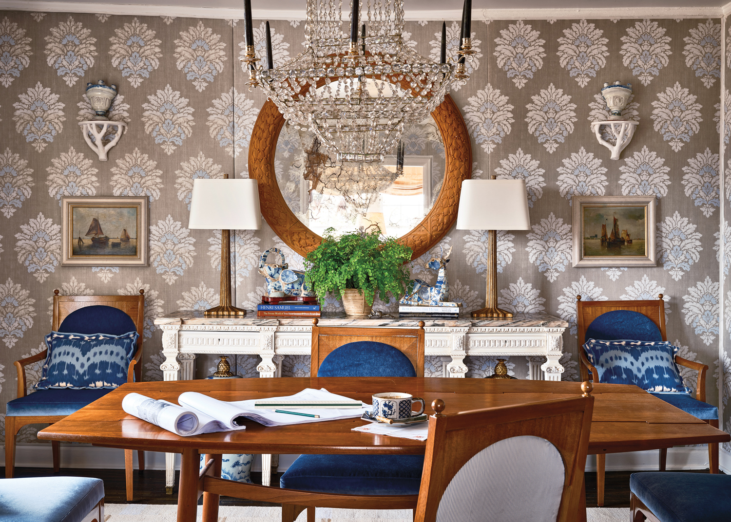 Dining room with wood table and chairs upholstered in dark blue fabric beneath a chandelier by Josh Pickering