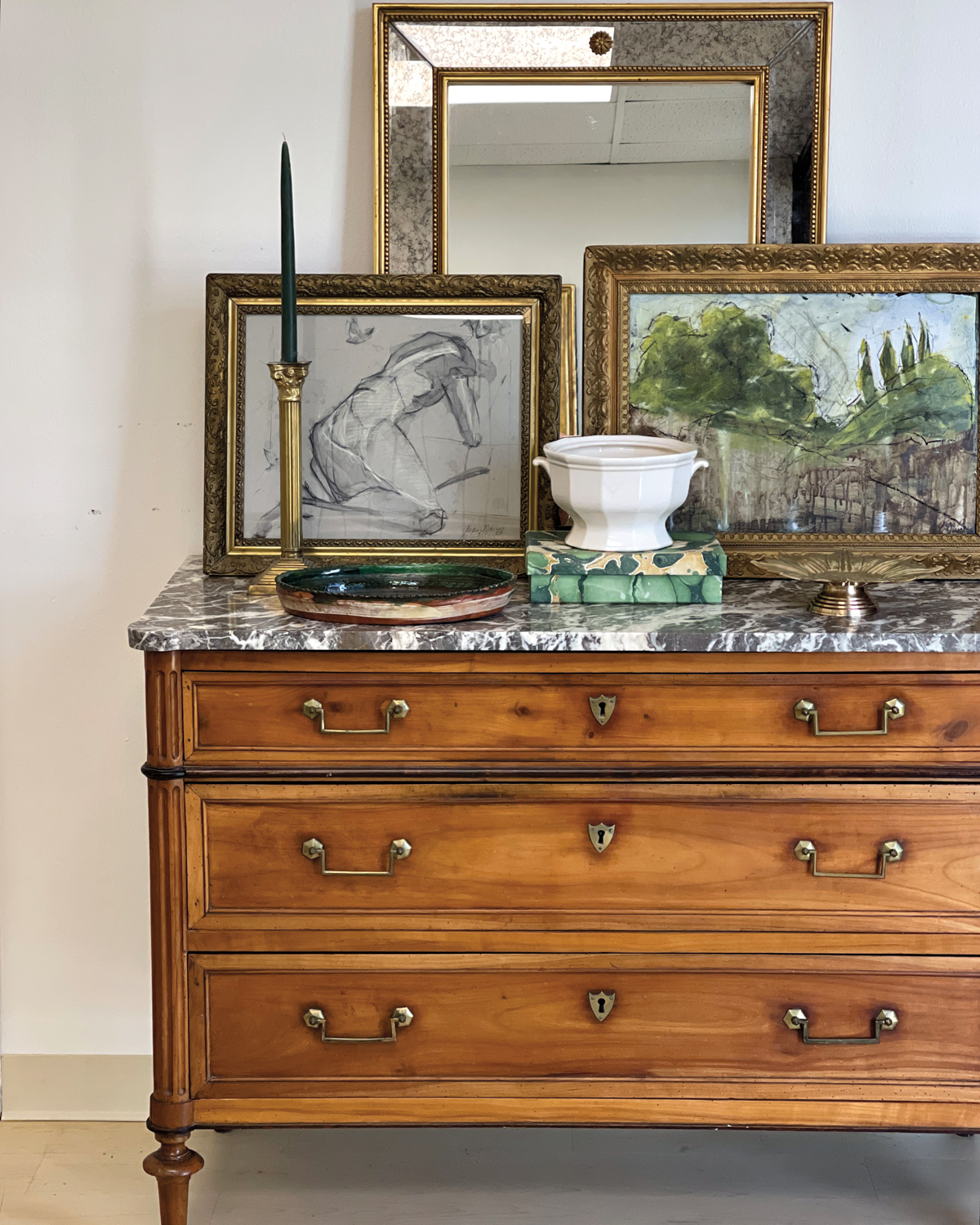 Low wooden dresser with a marble top styled with framed artworks and decorative dishes.