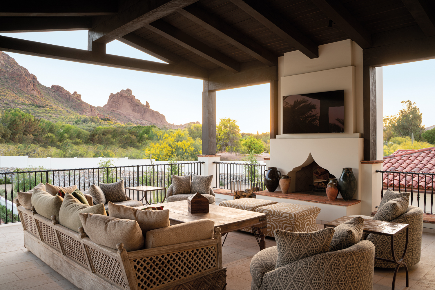 Covered outdoor lounge space with a TV over a fireplace, patterned taupe seating and mountain views