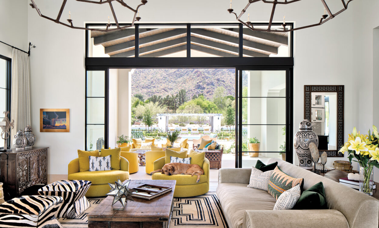Living room with two yellow swivel chairs, a taupe couch, zebra stools and glass doors opening to a patio