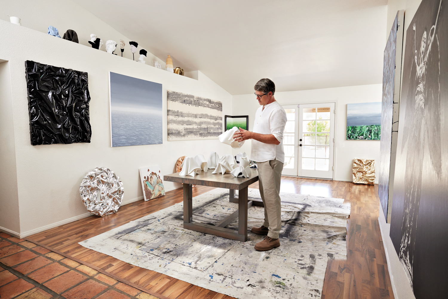 Jason Adkins stands in his studio holding a white sculpture and surrounded by artwork