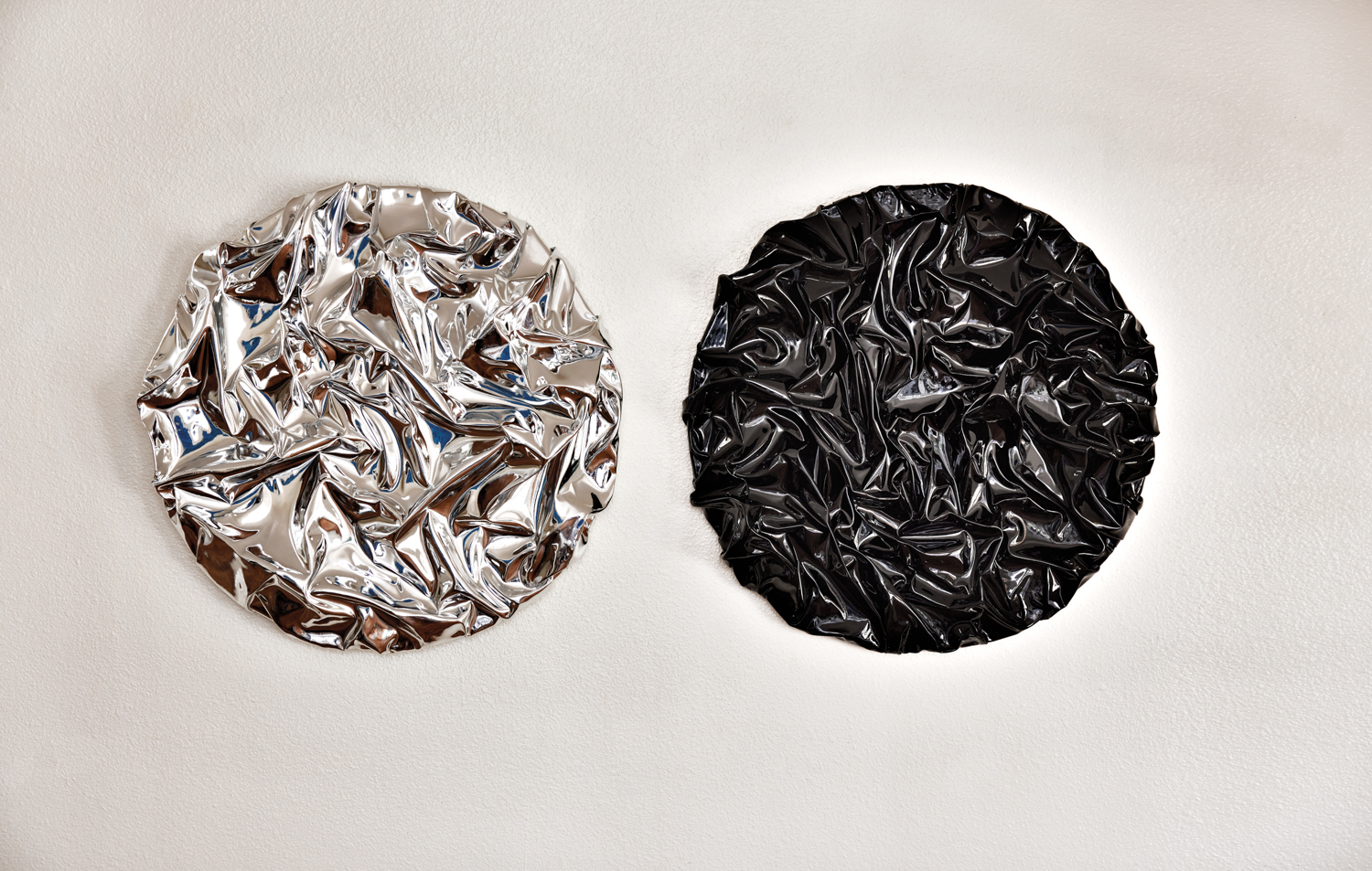 two metallic, textured, circular artworks, one silver and one black