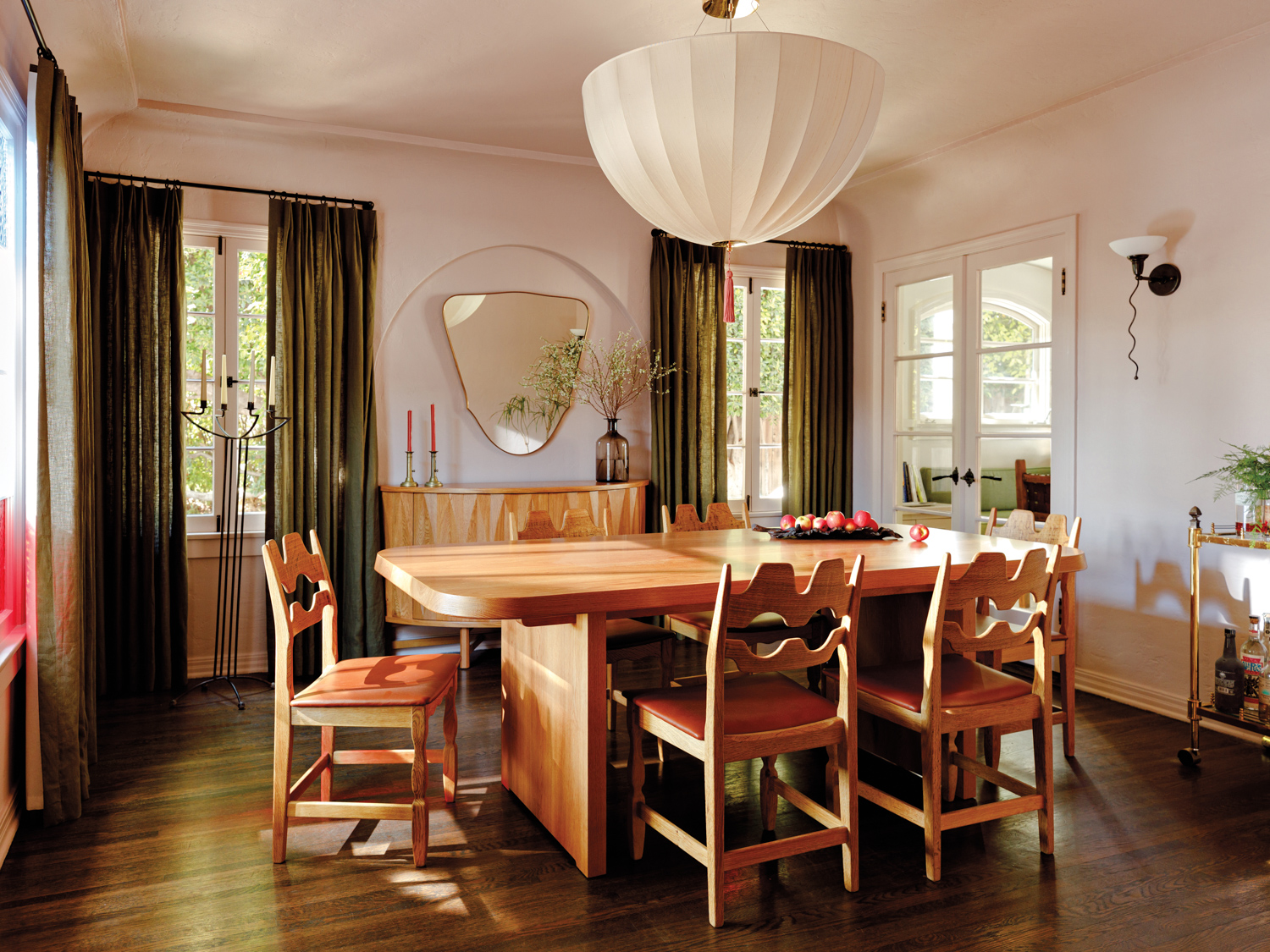 A dining room in a neutral palette with a natural-wood table and chairs and a semi-sphere white chandelier