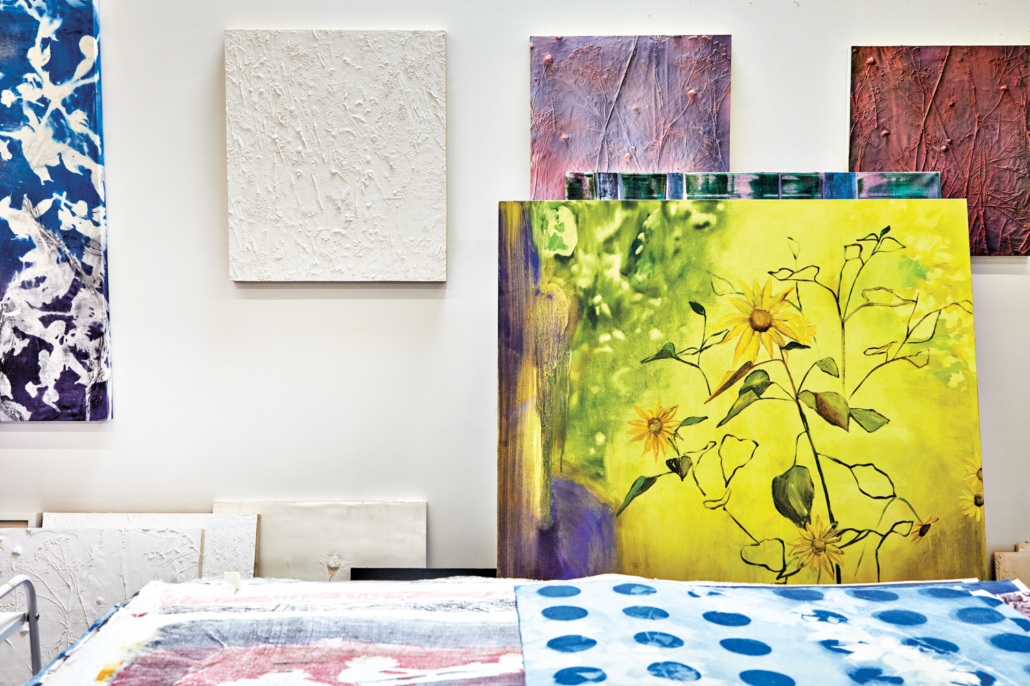 multiple floral artworks hanging and leaning on walls, and sitting on a table