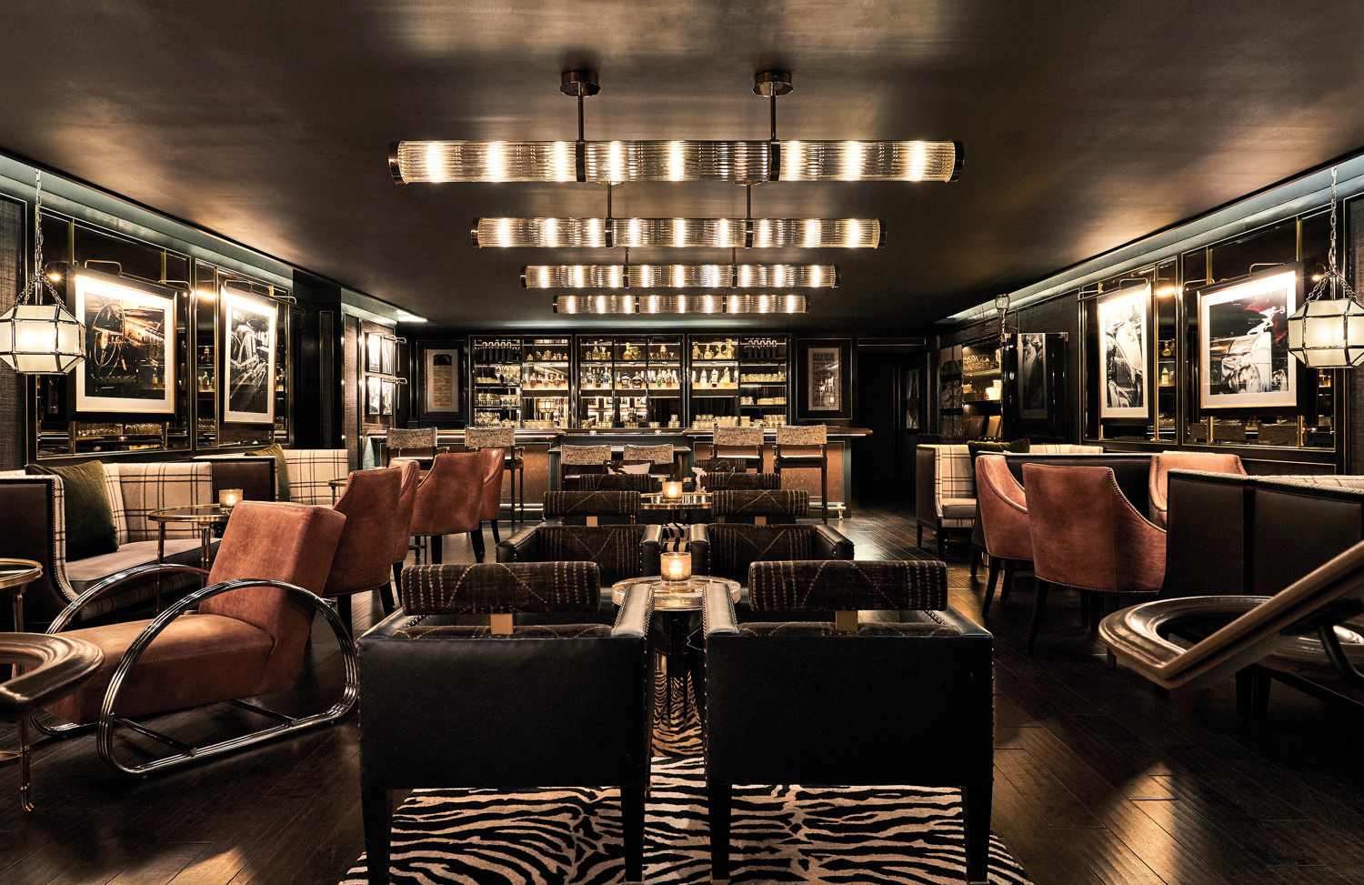 Cocktail lounge with dark seats, zebra-patterned rug and geometric lighting on a dark-painted ceiling