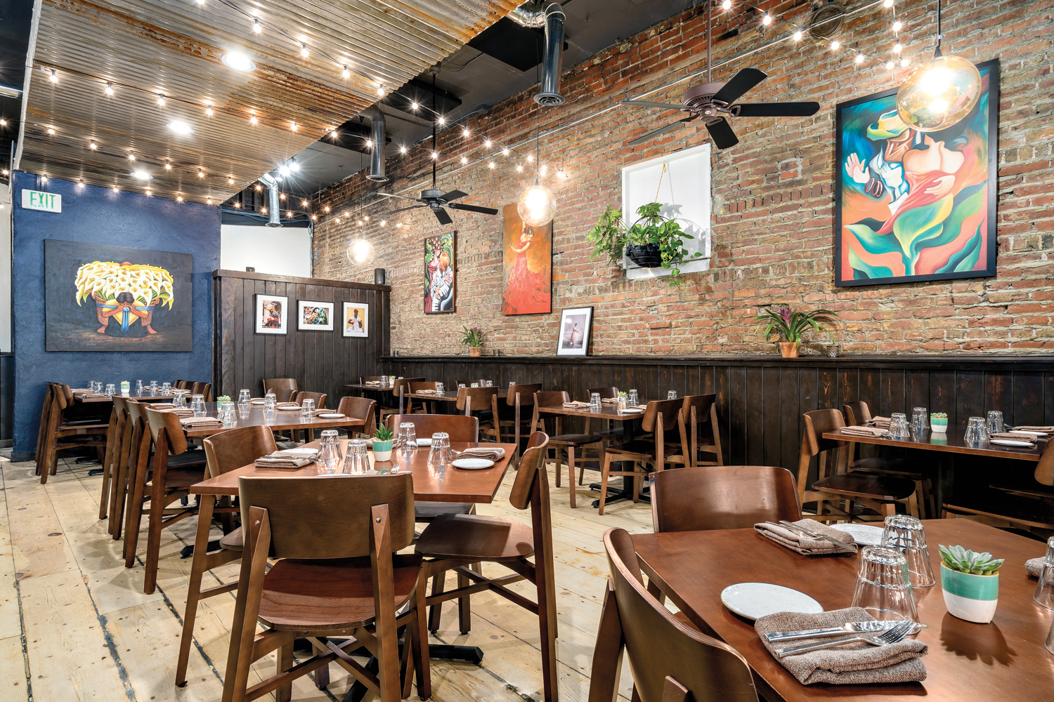 Restaurant with natural-brick wall, square tables, contemporary wall art and hanging twinkle lights