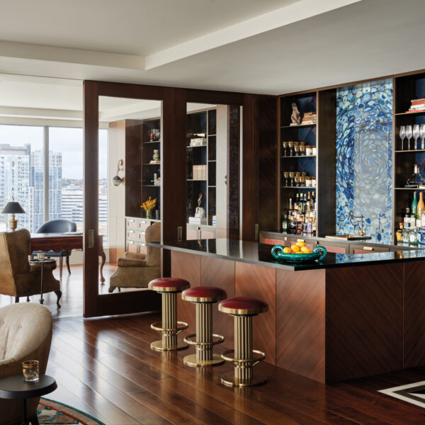 The bar area has a blue agate backsplash, upholstered stools and brass countertop in home by James Fung