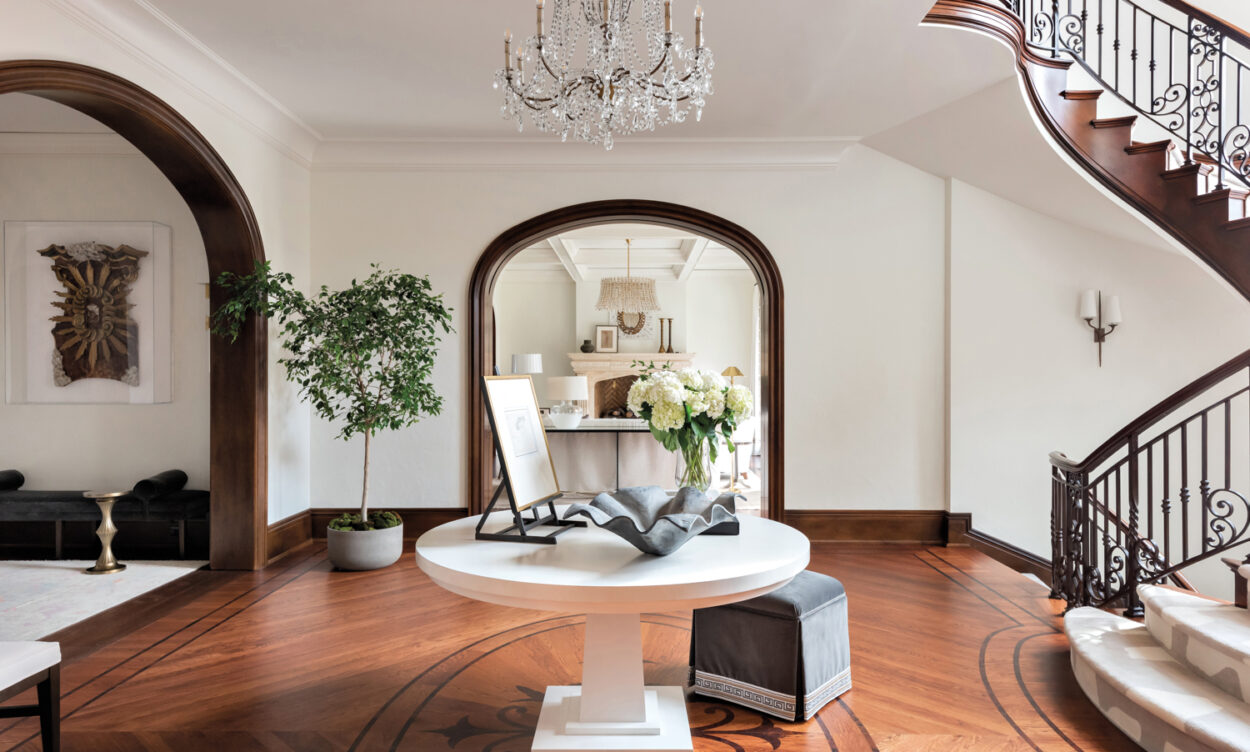 Central stair hall and foyer with wood floors, round center table, tree in corner and crystal chandelier