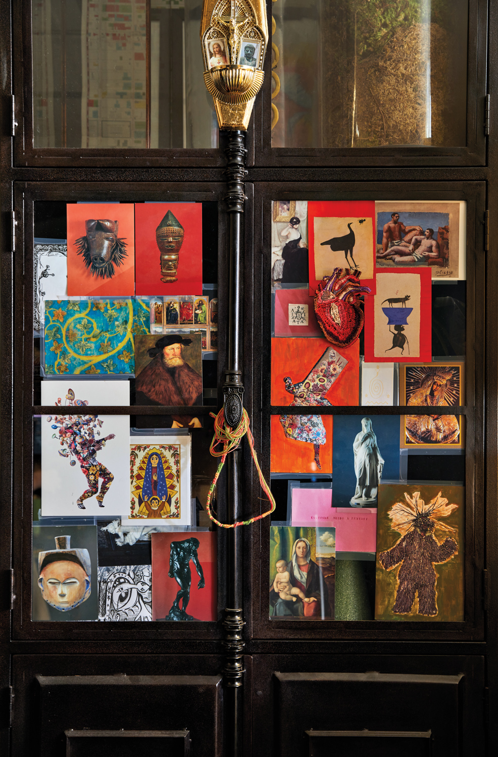 Dark metal cabinet decorated with small printed artworks, beads, insignia and other ephemera