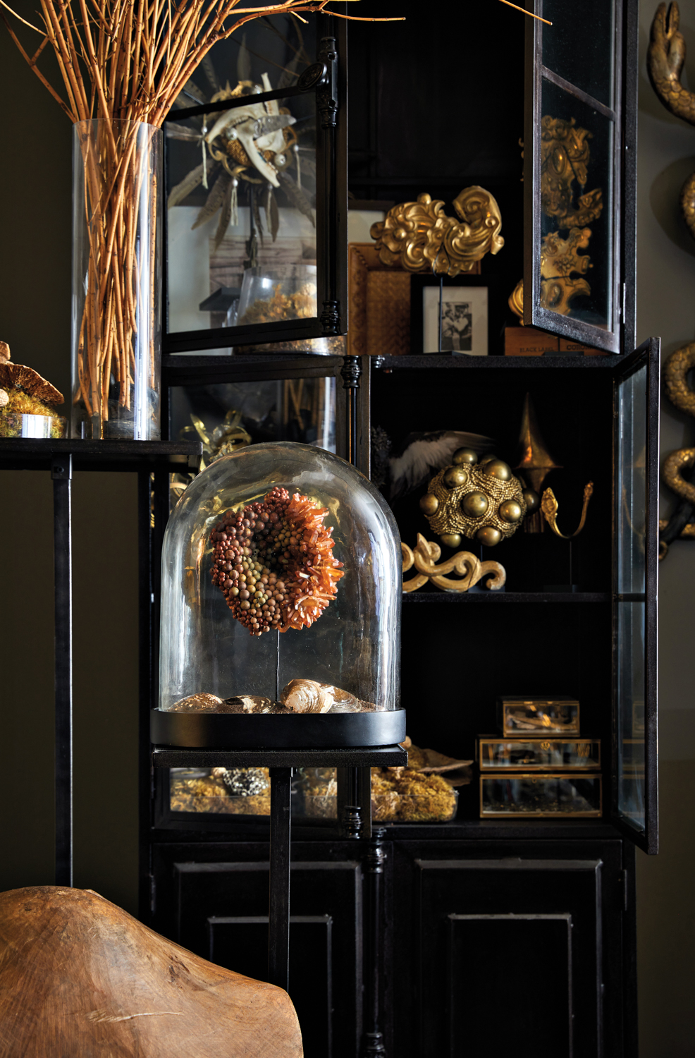 Dark metal cabinetry filled with gold-toned abstract sculptures, small photographs and preserved mosses