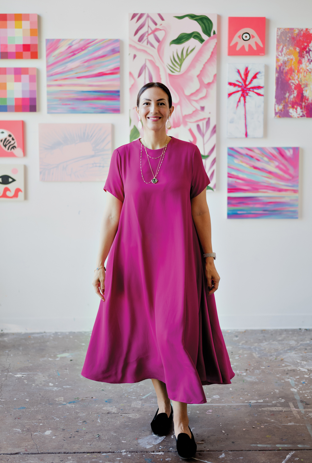 Gaby Viteri stands in a pink dress with a gallery wall of pink paintings behind her.