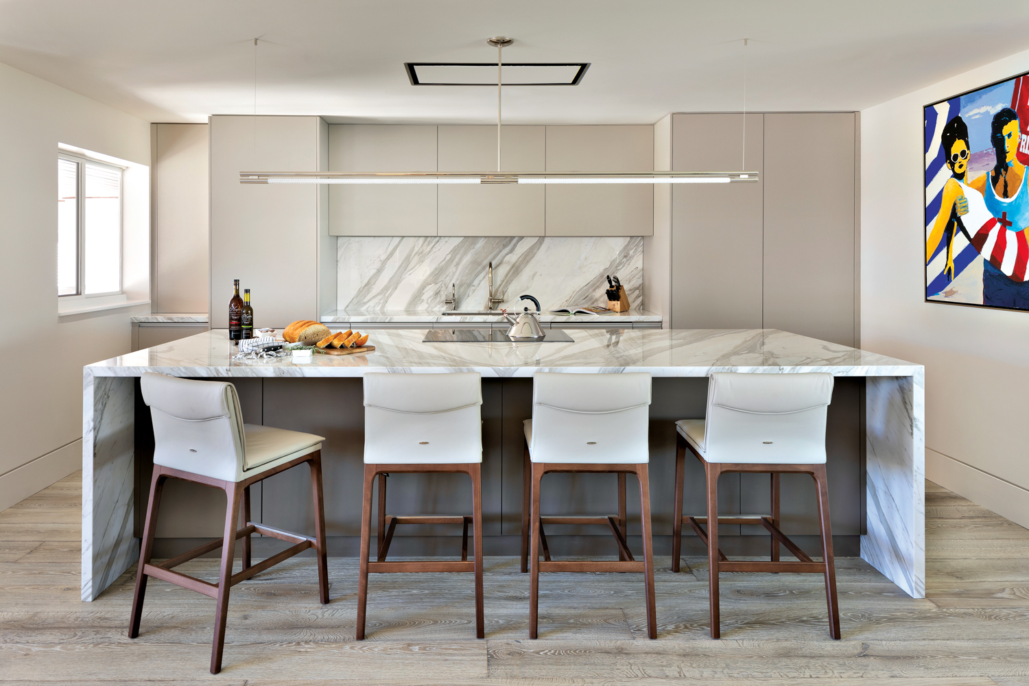 Sleek kitchen with white-marble waterfall island lined with highback chairs 