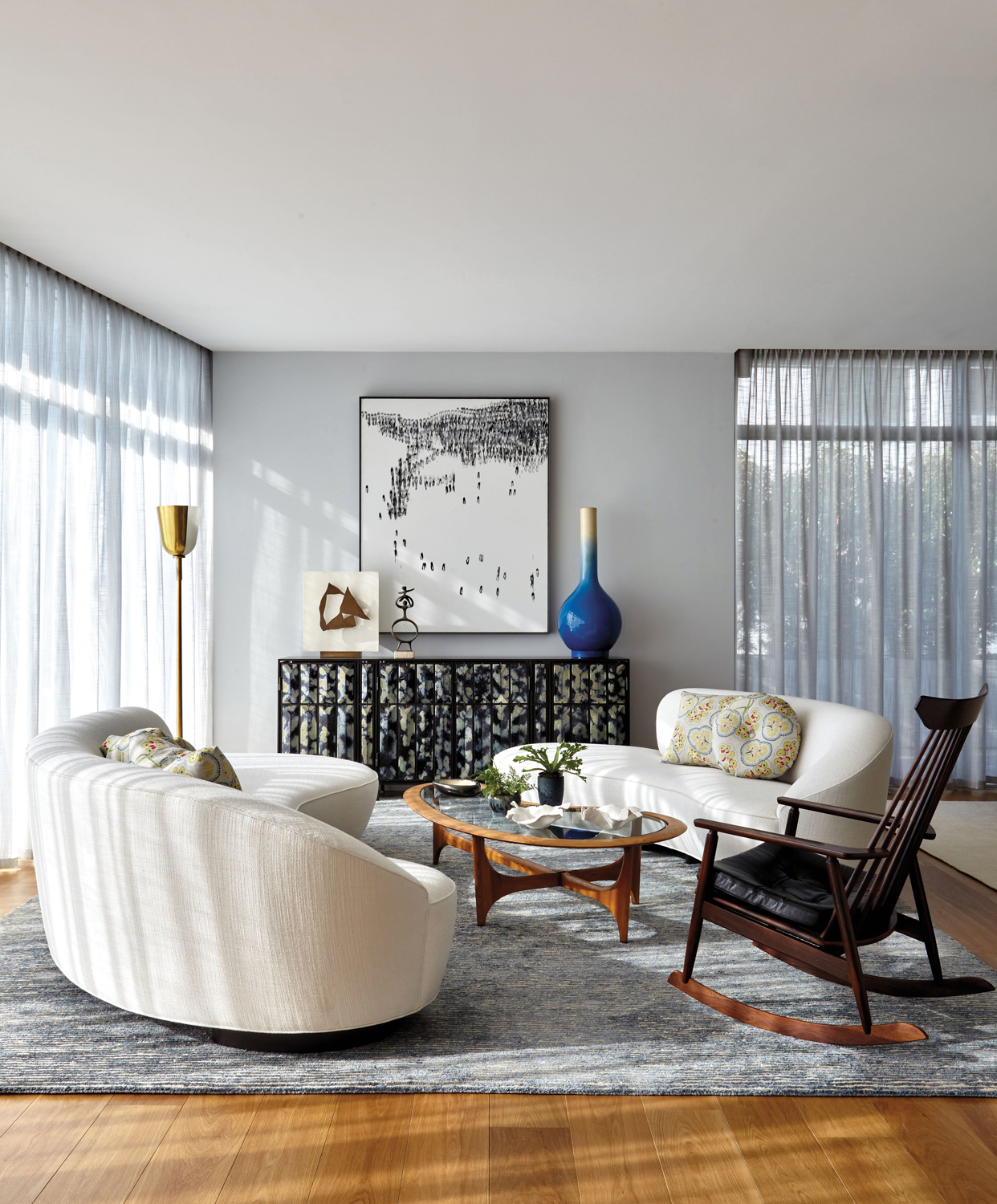Living space with curvy white sofas and a vintage rocking chair atop a grey area rug