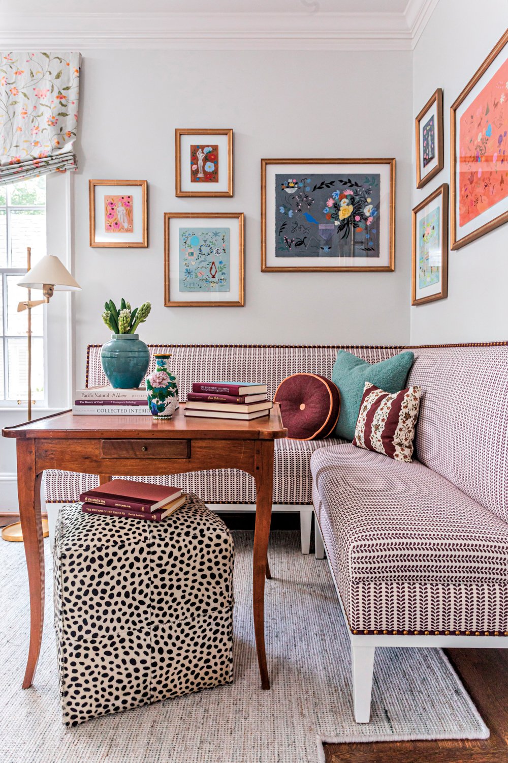L-shaped banquette forms reading nook with an antique wooden table and floral artworks framed above