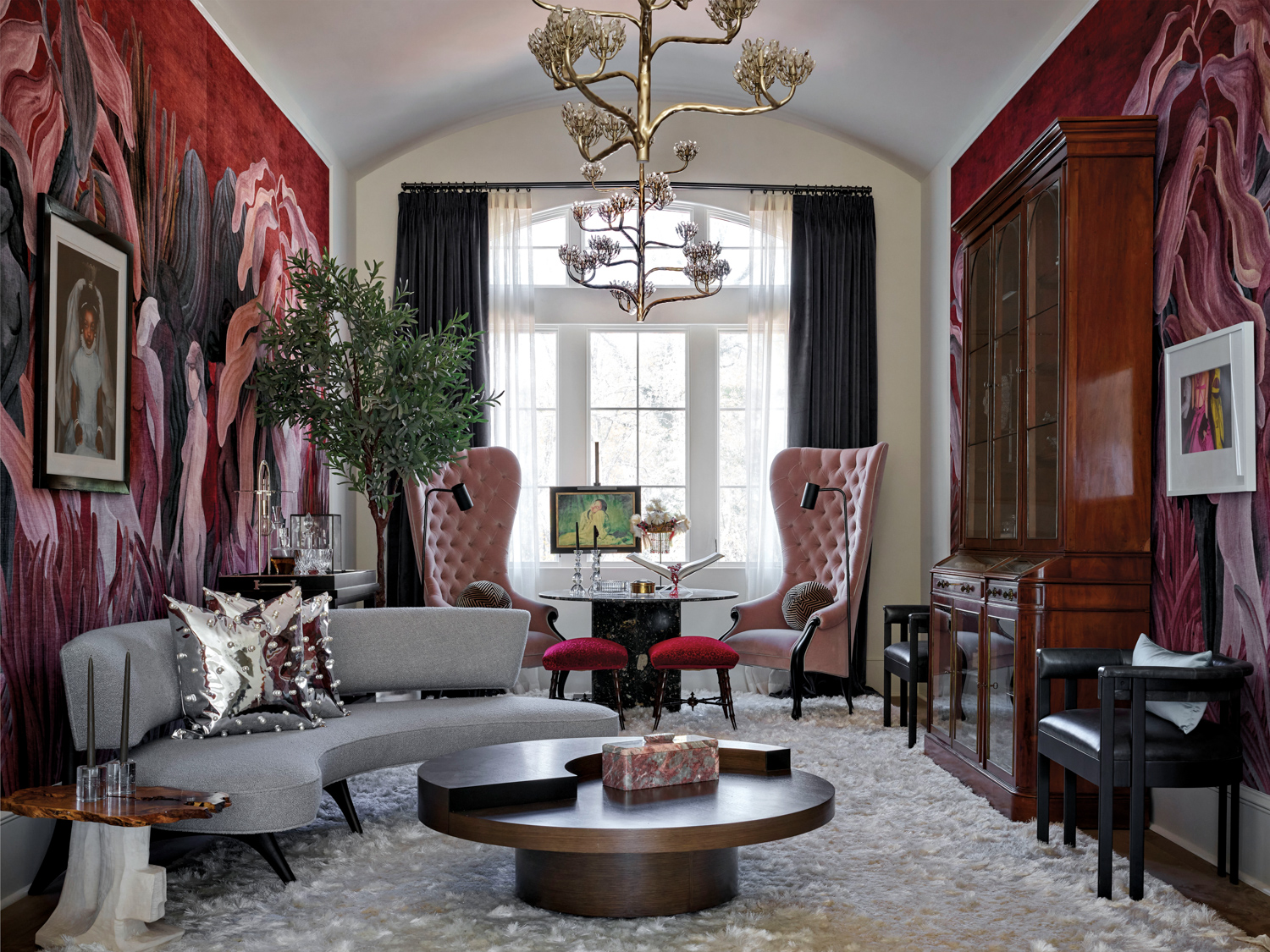 Living space with red wallcovering, sculptural light fixture, pink velvet armchairs and a curved gray sofa