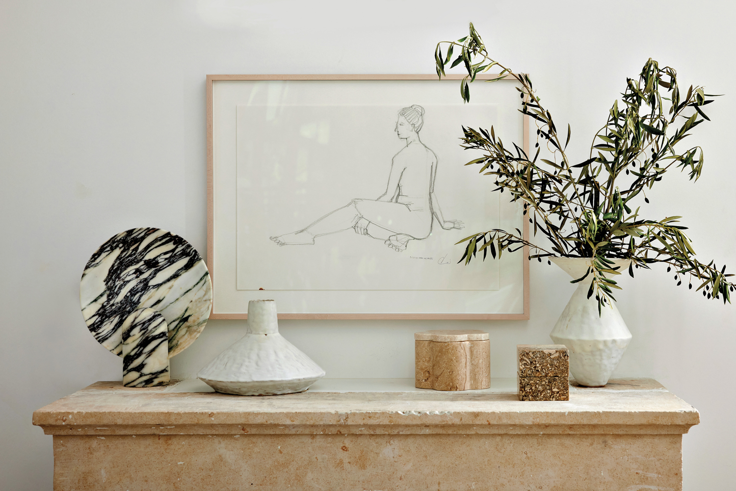 Figure drawing hanging above a stone console featuring vases and decorative pieces