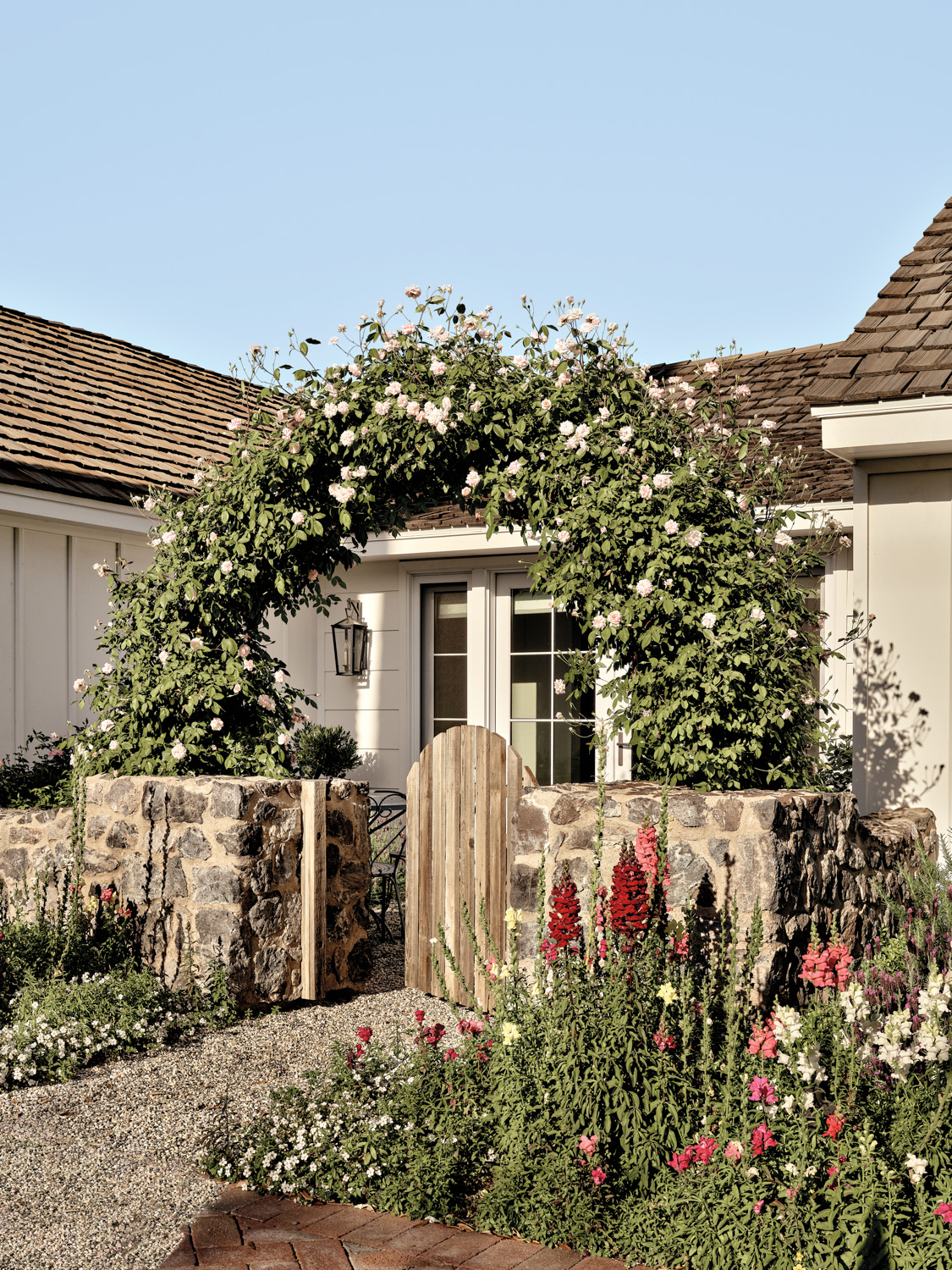 Pink Iceberg roses cover an archway at the entry gate of an English countryside-inspired cottage