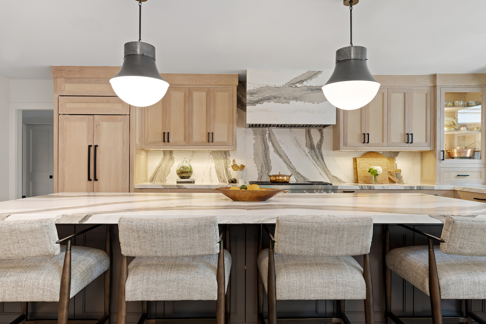 white kitchen with marble backsplash and light brown cabinets, silver pendant lighting