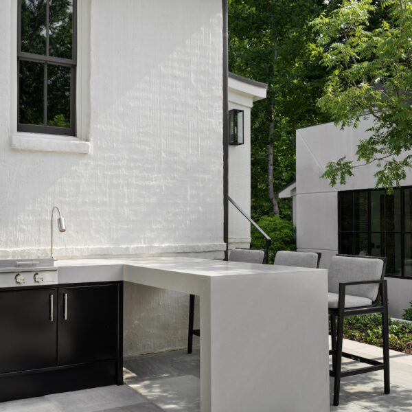 outdoor kitchen of a white home with pizza oven and built in grill and black bar stools
