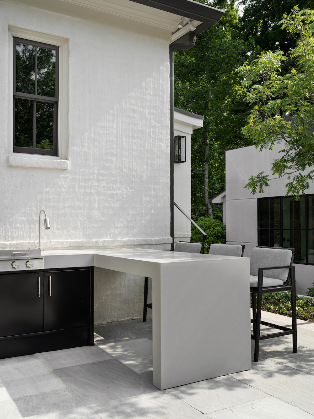 outdoor kitchen of a white home with pizza oven and built in grill and black bar stools