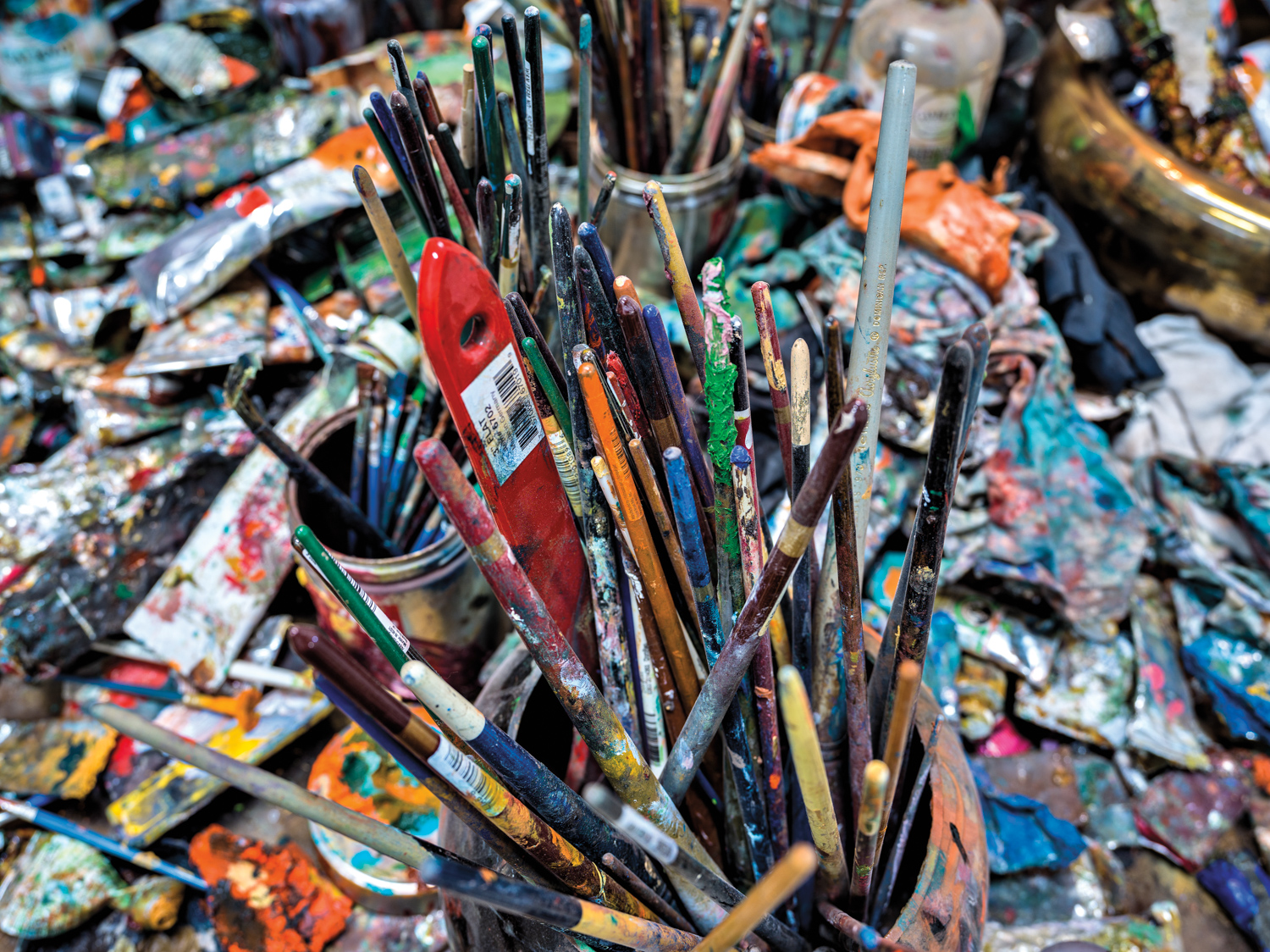 An artist workspace filled with an array of paintbrushes, razors, and palette knives