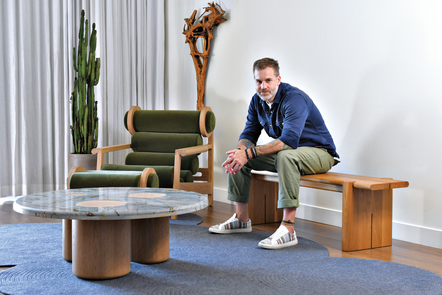 Todd Hewitt sitting on a bench beside a coffee table and a chaise from his studio, Last Ditch Design