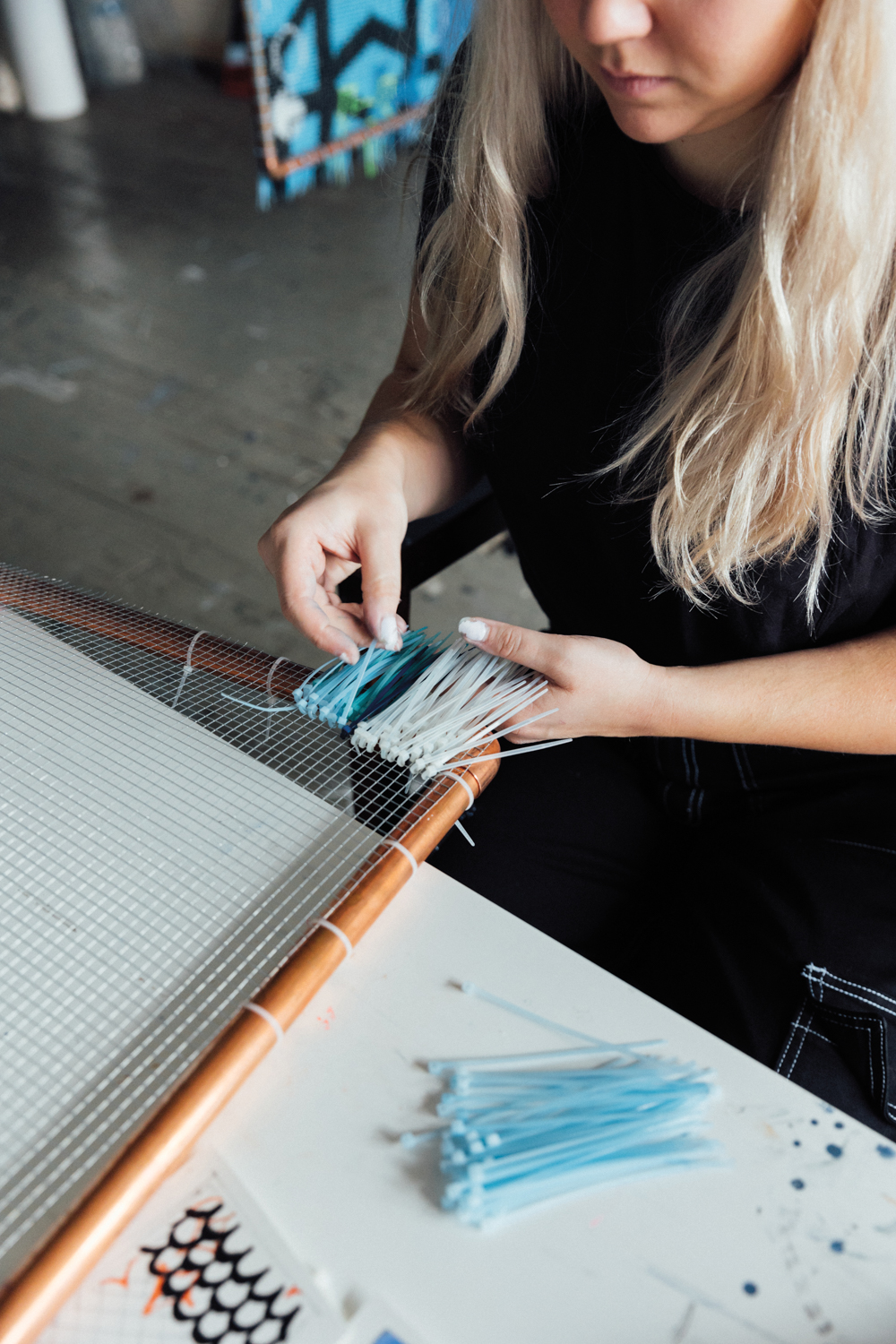woman weaving blue and white zip ties on chicken wire