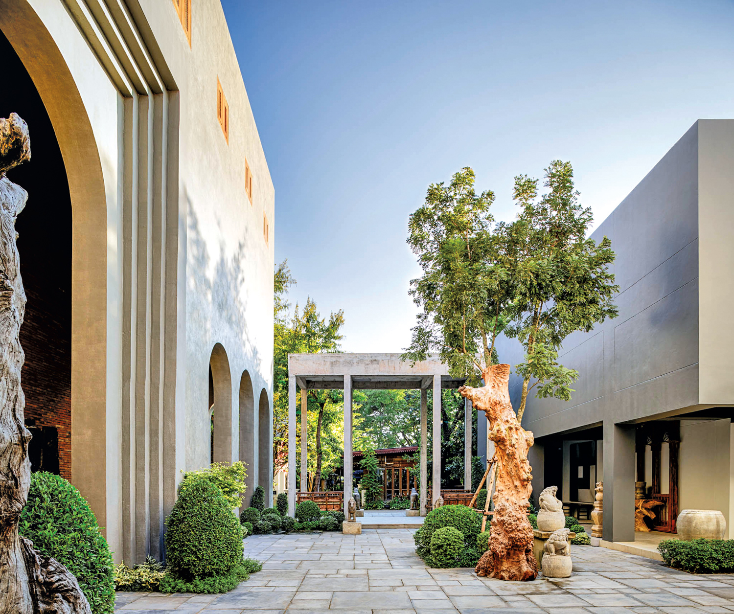 Courtyard with lush green shrubbery and trees accented by stone sculptures