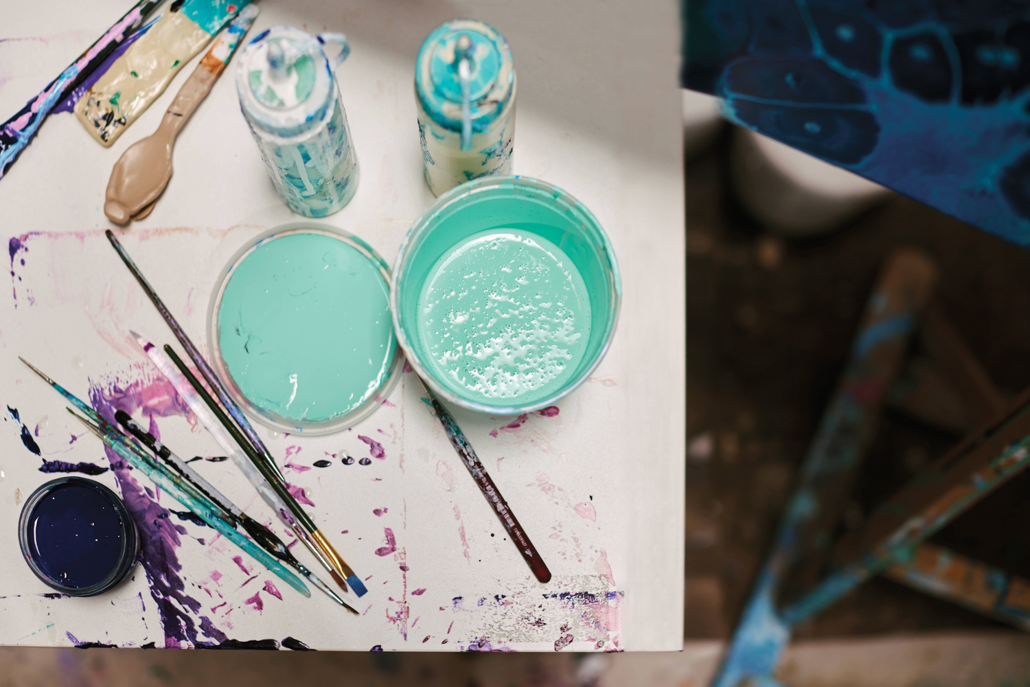 bucket of teal paint with lid off, set of small paint brushes and spray paint cans