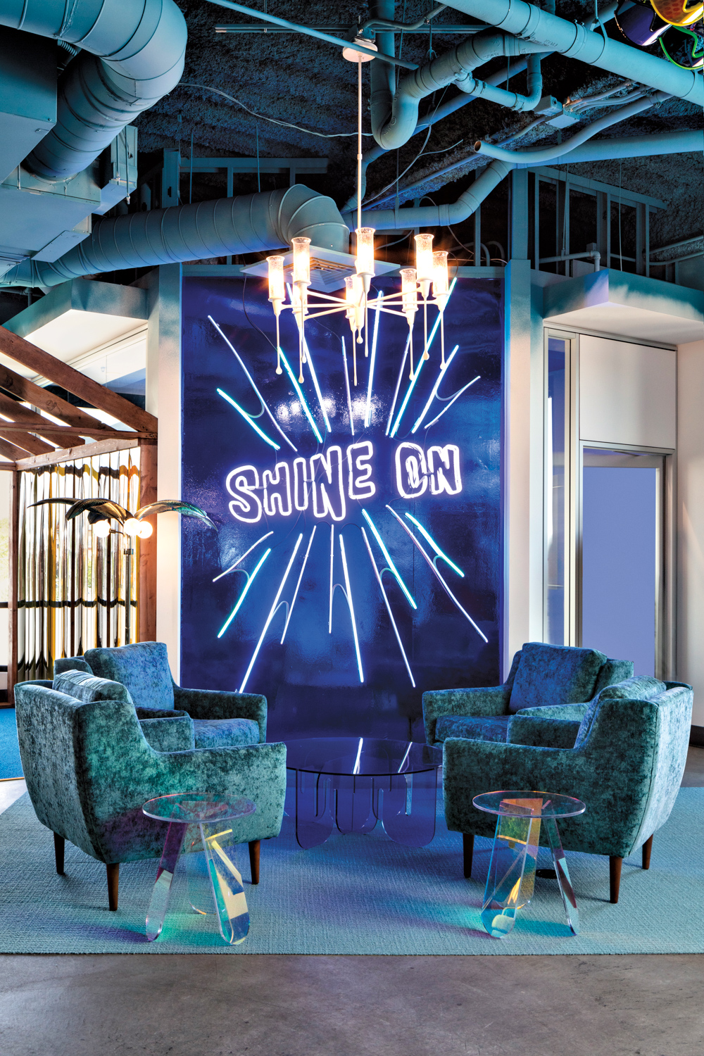 Four blue armchairs against an electric-blue wall with a neon signs that reads "Shine On."