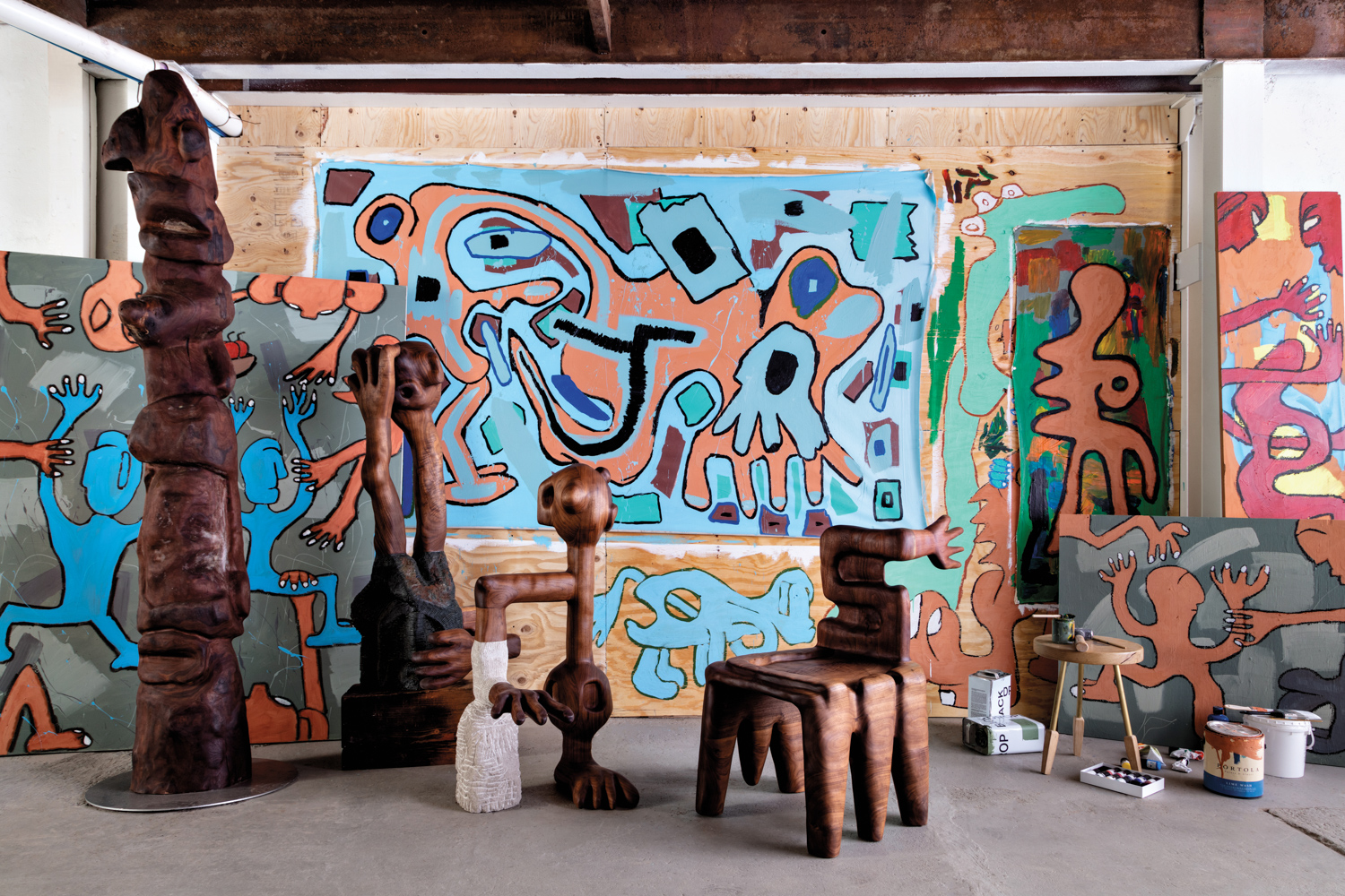 Wood sculptures by Casey McCafferty surrounded by colorful abstract murals on his studio's walls